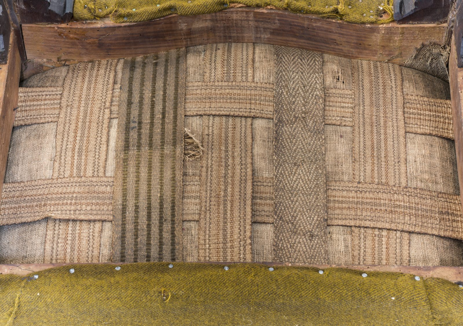 Underside of a window seat showing original webbing and hay and meadow grass filling
